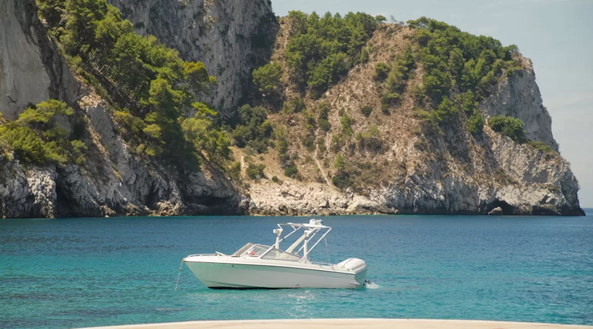 A small white boat moored in a turquoise cove below the Taormina cliffs during a half day boat tour