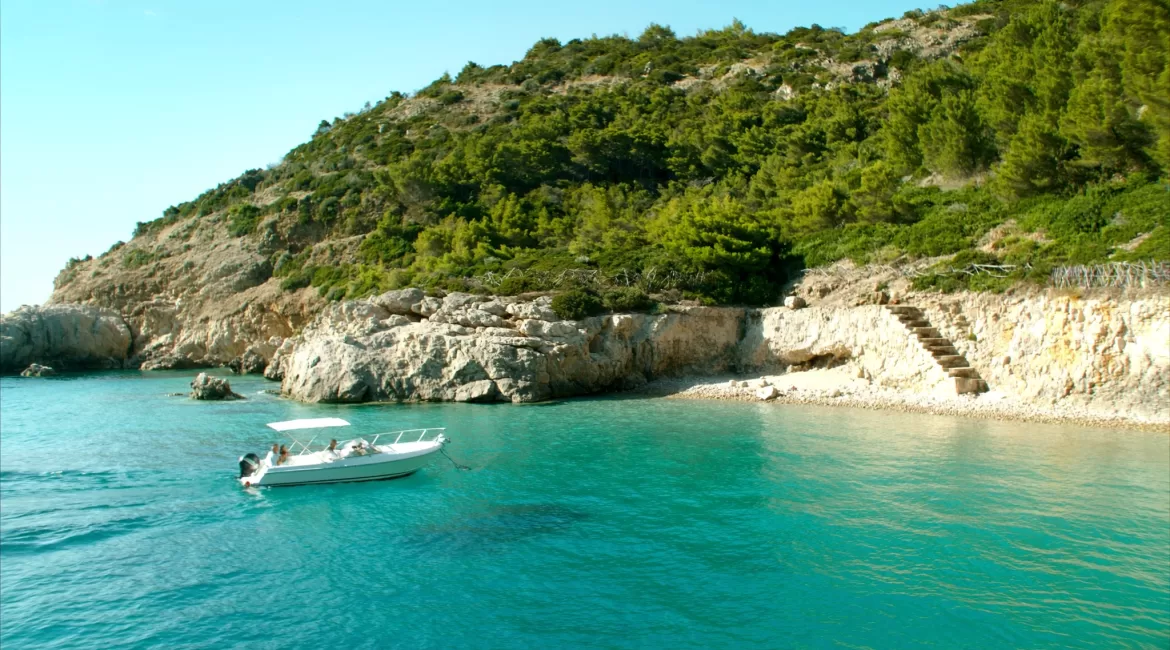 A small white sea taxi boat in a turquoise cove near Taormina with steps down to a pebble beach