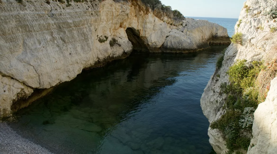 A narrow hidden cove between pale limestone cliffs near Taormina with clear green water