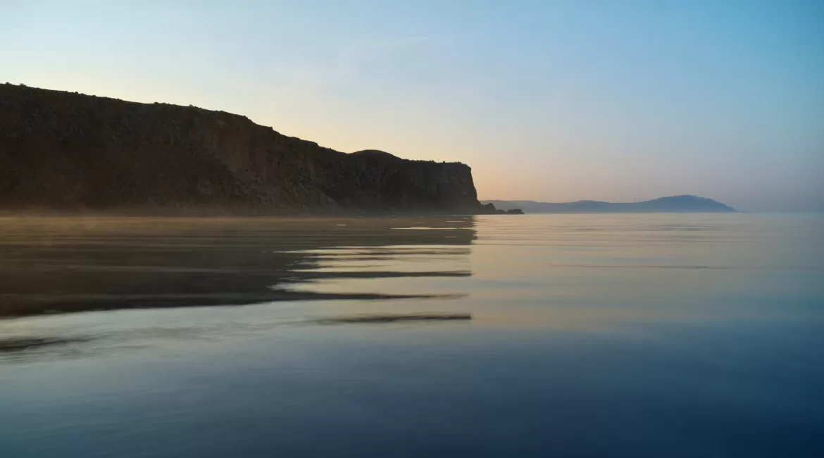 Dawn light on a mirror-calm sea below the cliffs near Taormina, the best time of day for a boat tour