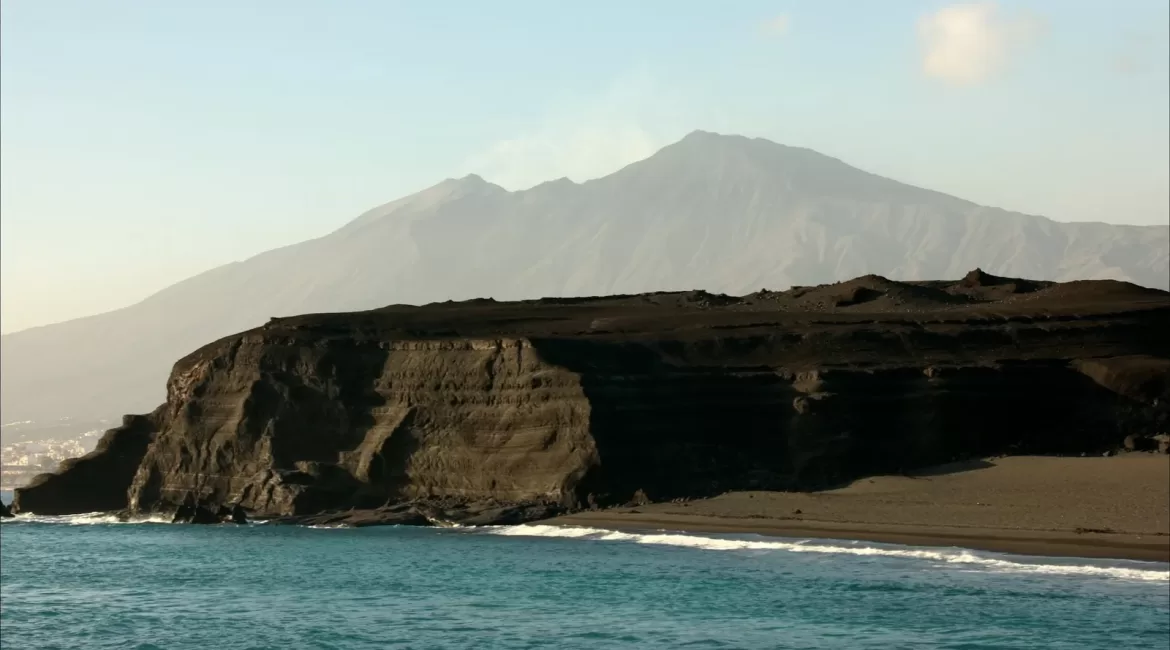 Giardini Naxos by boat: the black lava headland of Capo Schiso with Etna rising behind it
