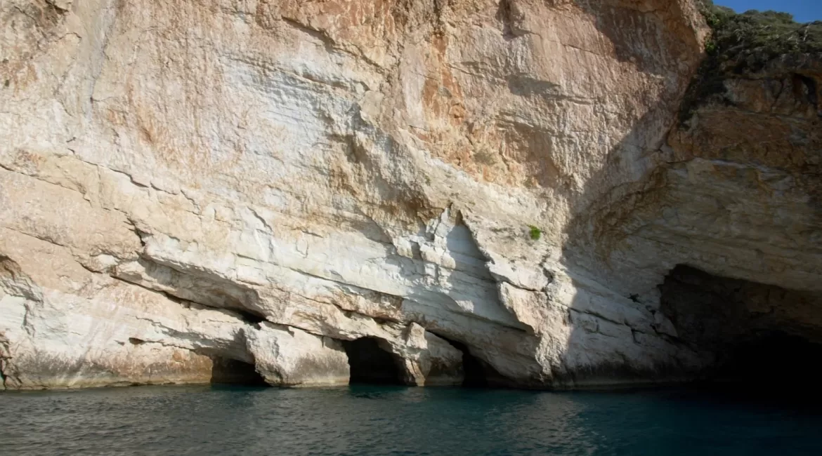 The Taormina cliffs and sea caves: a tall pale limestone face with dark cave openings at the waterline