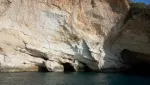 The Taormina cliffs and sea caves: a tall pale limestone face with dark cave openings at the waterline
