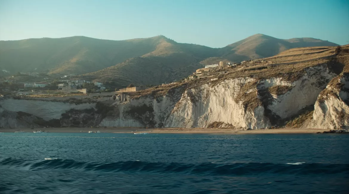 Taormina in October seen from the water, with soft autumn light on the cliffs and an empty coastline